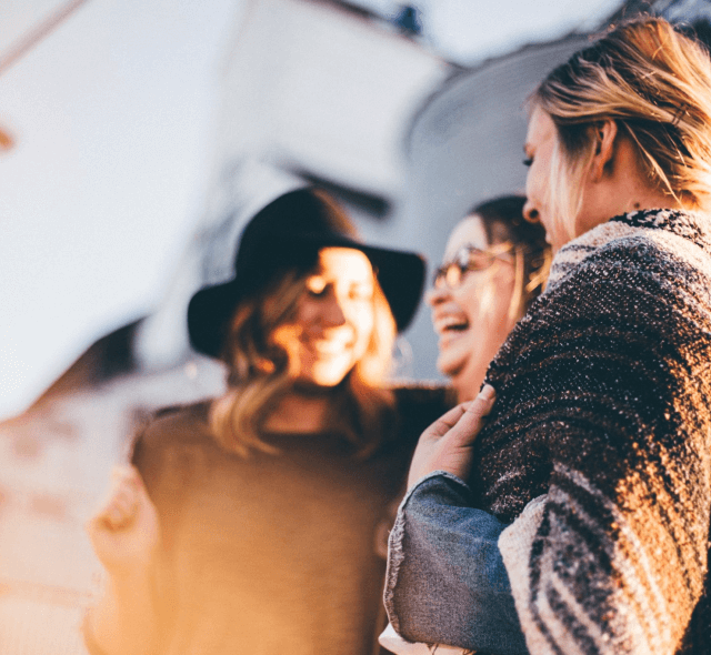 three women laughing and holding each other during an outing at Capo Beach Recovery