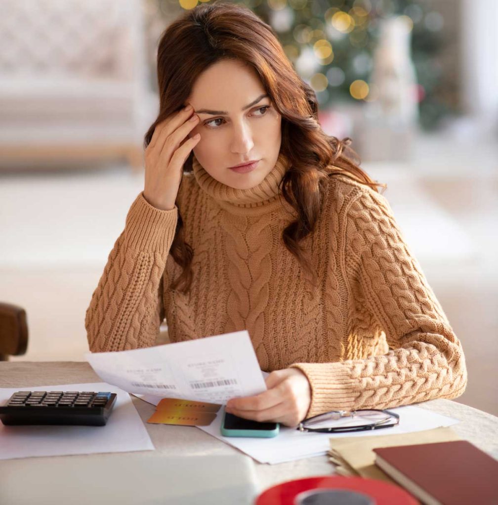 woman sitting at a desk with her hand on her forehead trying to understand the complexity of financial stress during the holidays