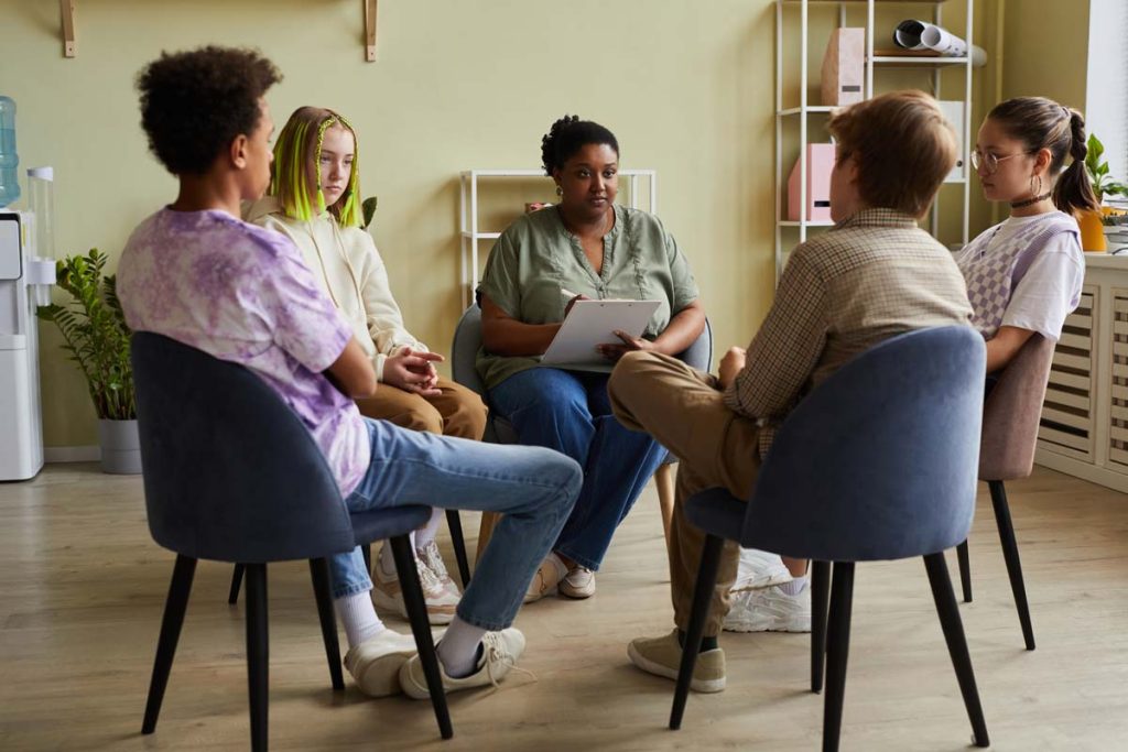 Signs of Alcohol Addiction: A Comprehensive Guide 6 Adolescent group therapy session with a licensed therapist taking notes and trying to help them break their addictions