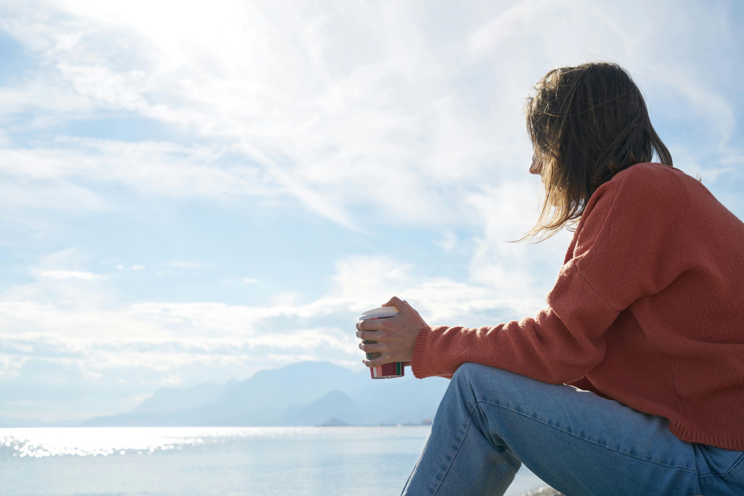 Person sitting by the ocean holding a coffee cup, reflecting on life and recovery near Capistrano Beach in Orange County, California.