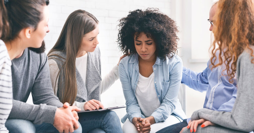 Group of people offering comfort and support to a woman during addiction counseling at Capo Beach Recovery in San Juan Capistrano, California, highlighting compassion in recovery from melatonin or prescription drug misuse.