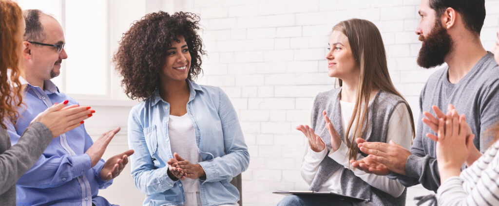 Group of people smiling and supporting each other during a therapy session at Capo Beach Recovery in San Juan Capistrano, California, representing community and encouragement in addiction recovery.