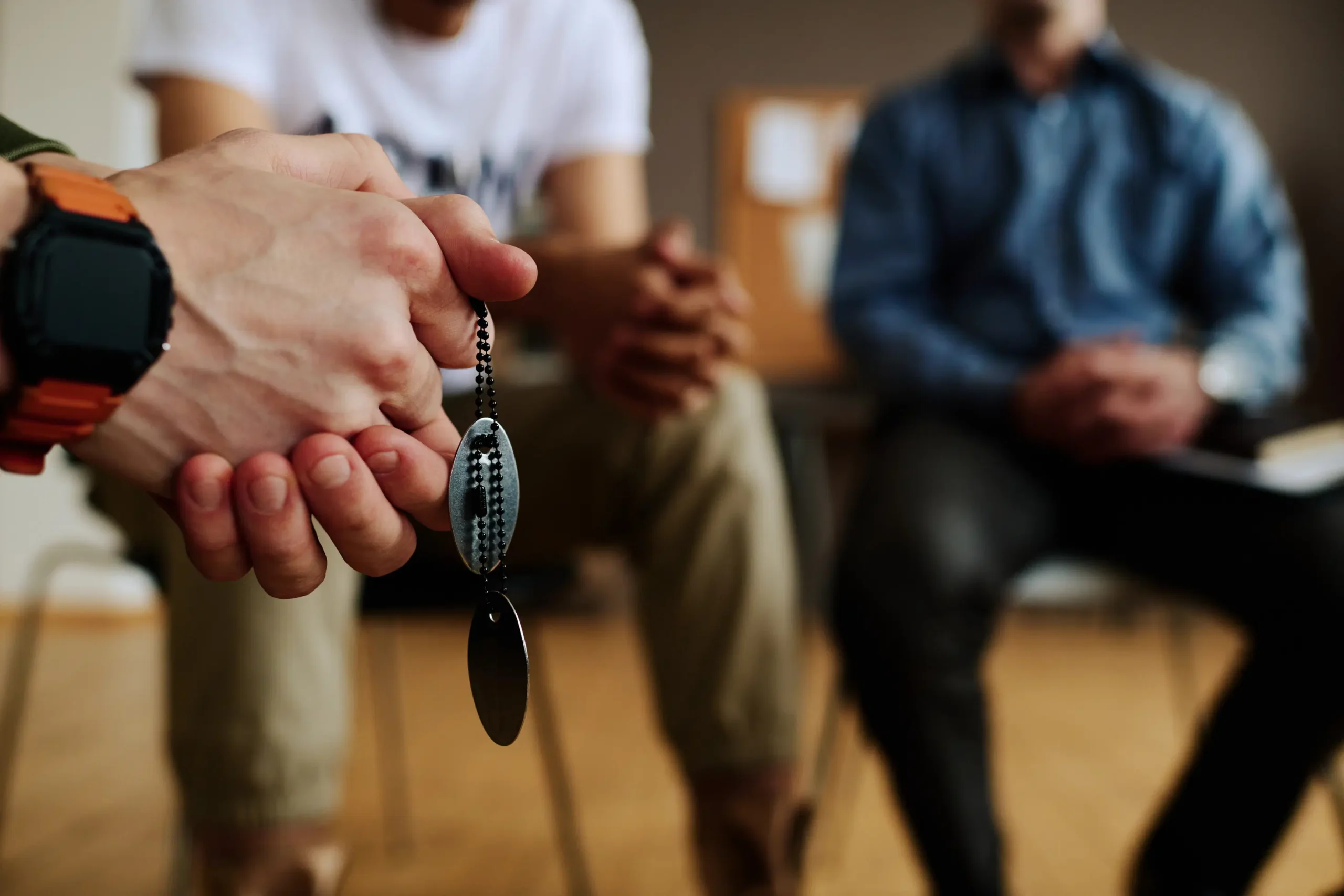 Close-up of a person holding dog tags during a group therapy session at Capo Beach Recovery in San Juan Capistrano, California, symbolizing hope and healing from addiction and mental health challenges.