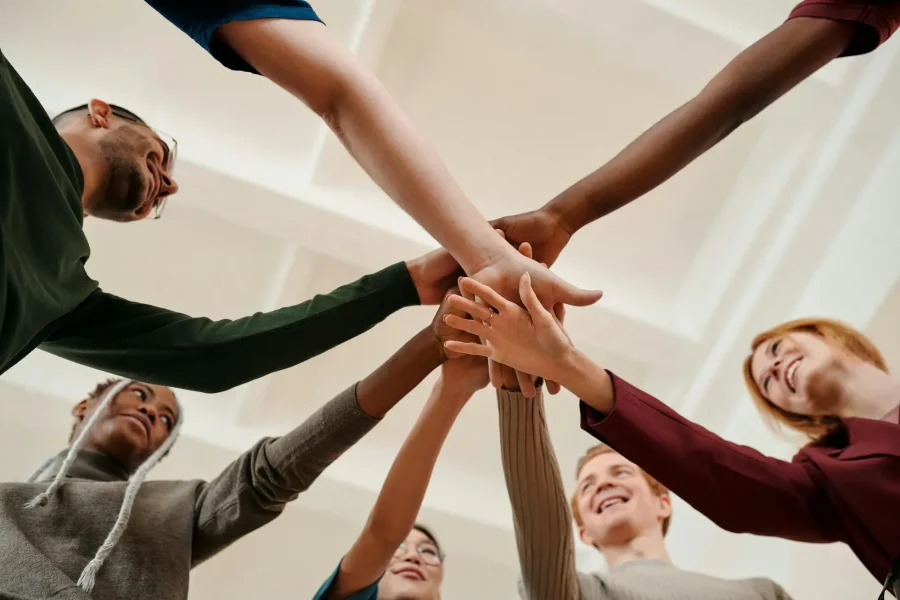 Group of people smiling and stacking hands together in unity at Capo Beach Recovery in San Juan Capistrano, California, representing teamwork and support in addiction recovery.